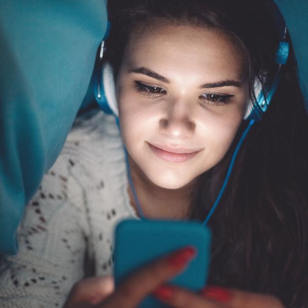 Pige i seng med hovedtelefoner og mobil